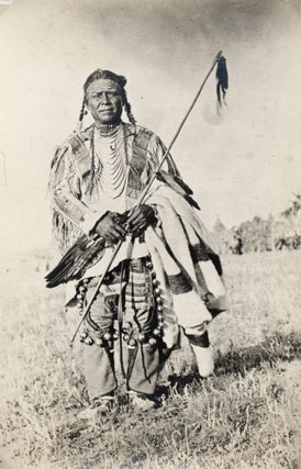 Item #365589 [Standing portrait of a Blackfeet man in a painted deerskin shirt, with dancing...